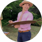 Seattle live wedding painter Chris Cook smiling and painting at a wedding wearing a hat and pink shirt.